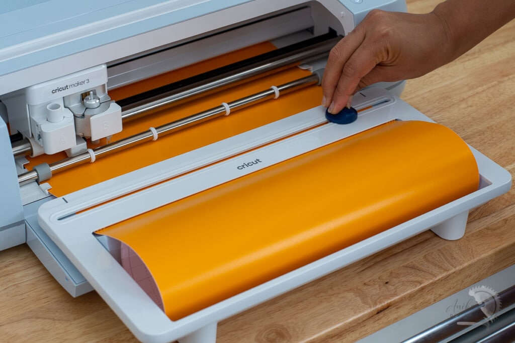 Cricut Paper holder with Orange vinyl and woman trimming off the vinyl with built in trimmer
