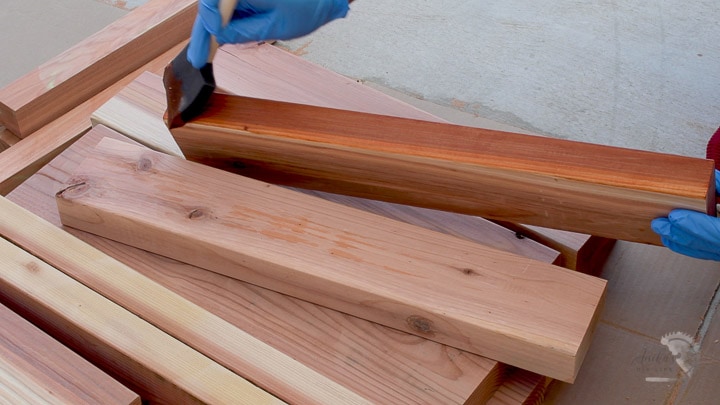 woman staining redwood boards to build a DIY outdoor box