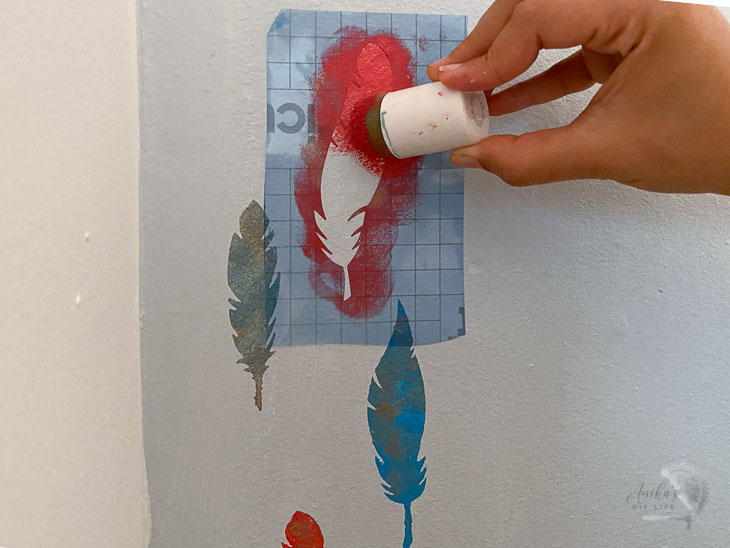 applying red paint to feather stencil on wall