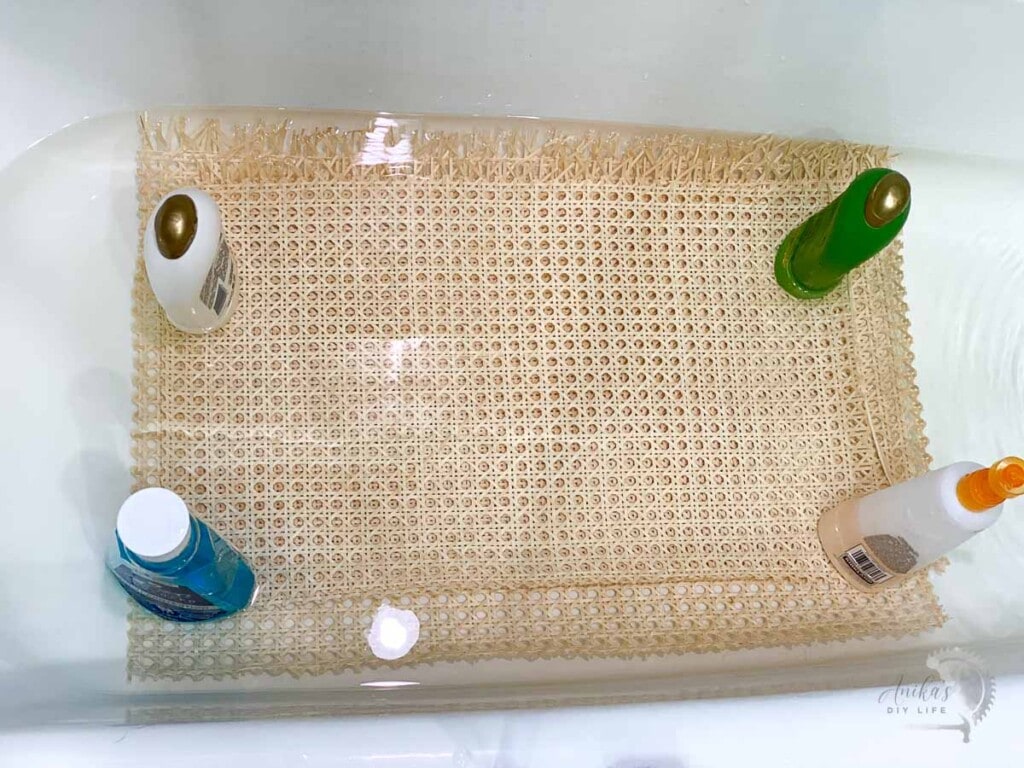 Cane webbing being soaked in hot water in bathtub and held down by bottles