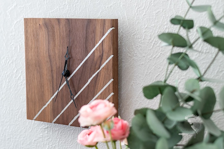 DIY wood wall clock with metal inlay next to pink roses