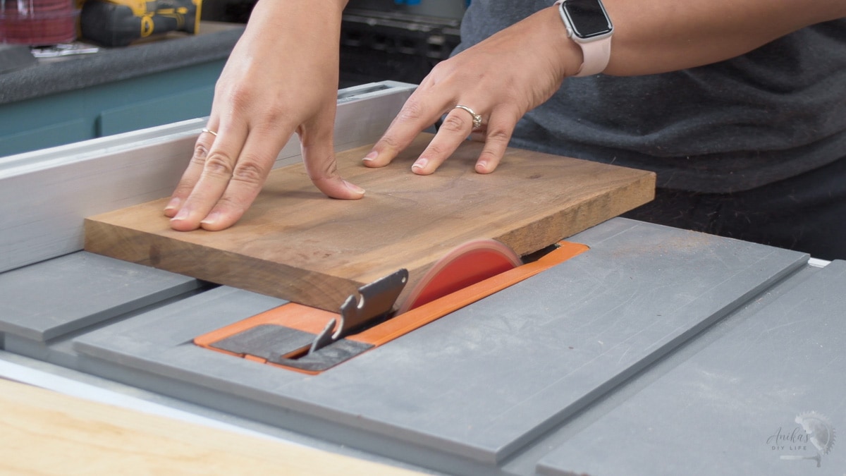 woman trimming off walnut board on table saw to make a cutting board