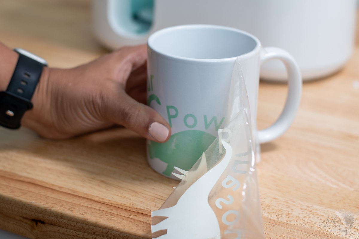 peeling away infusible ink sheet to reveal green design on white mug
