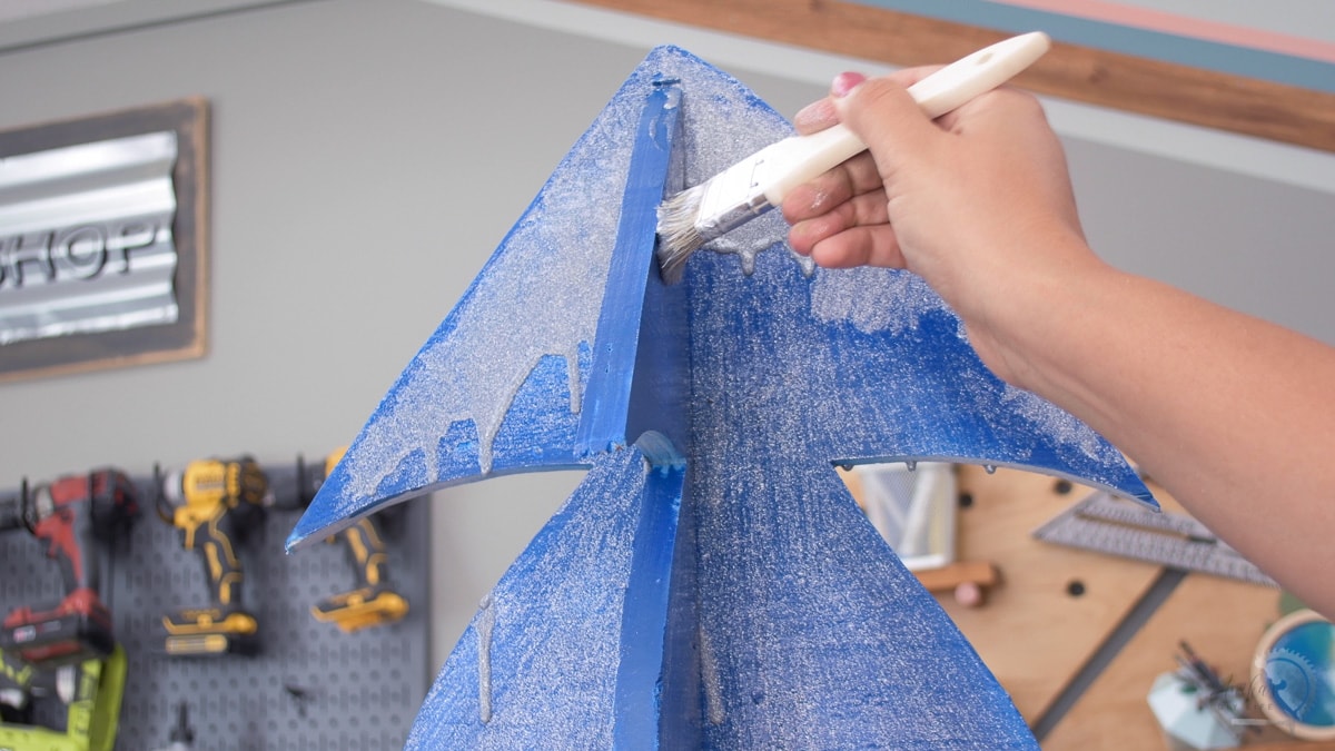 Applying glitter paint to a blue plywood Christmas tree
