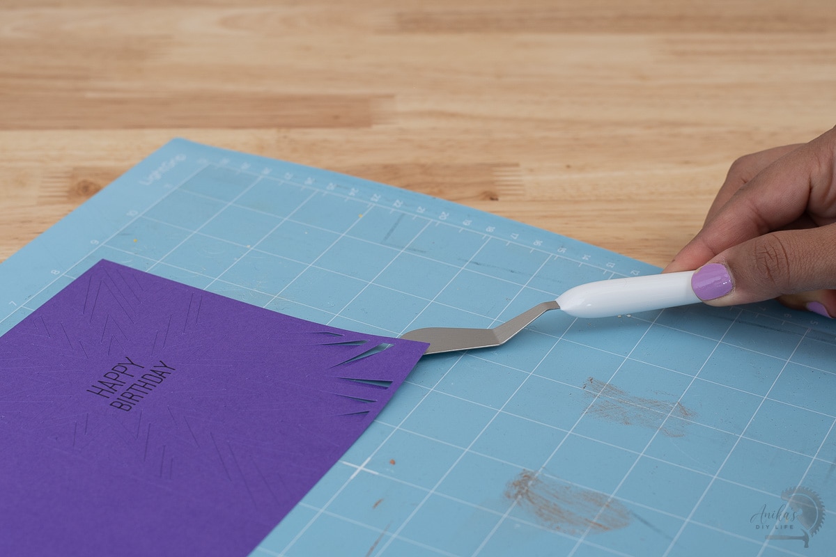 using a spatula to lift up paper from mat