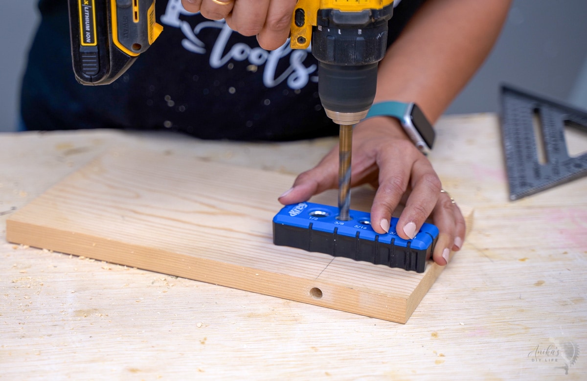 Woman drilling hole into the surface of a  board using the drilling guide